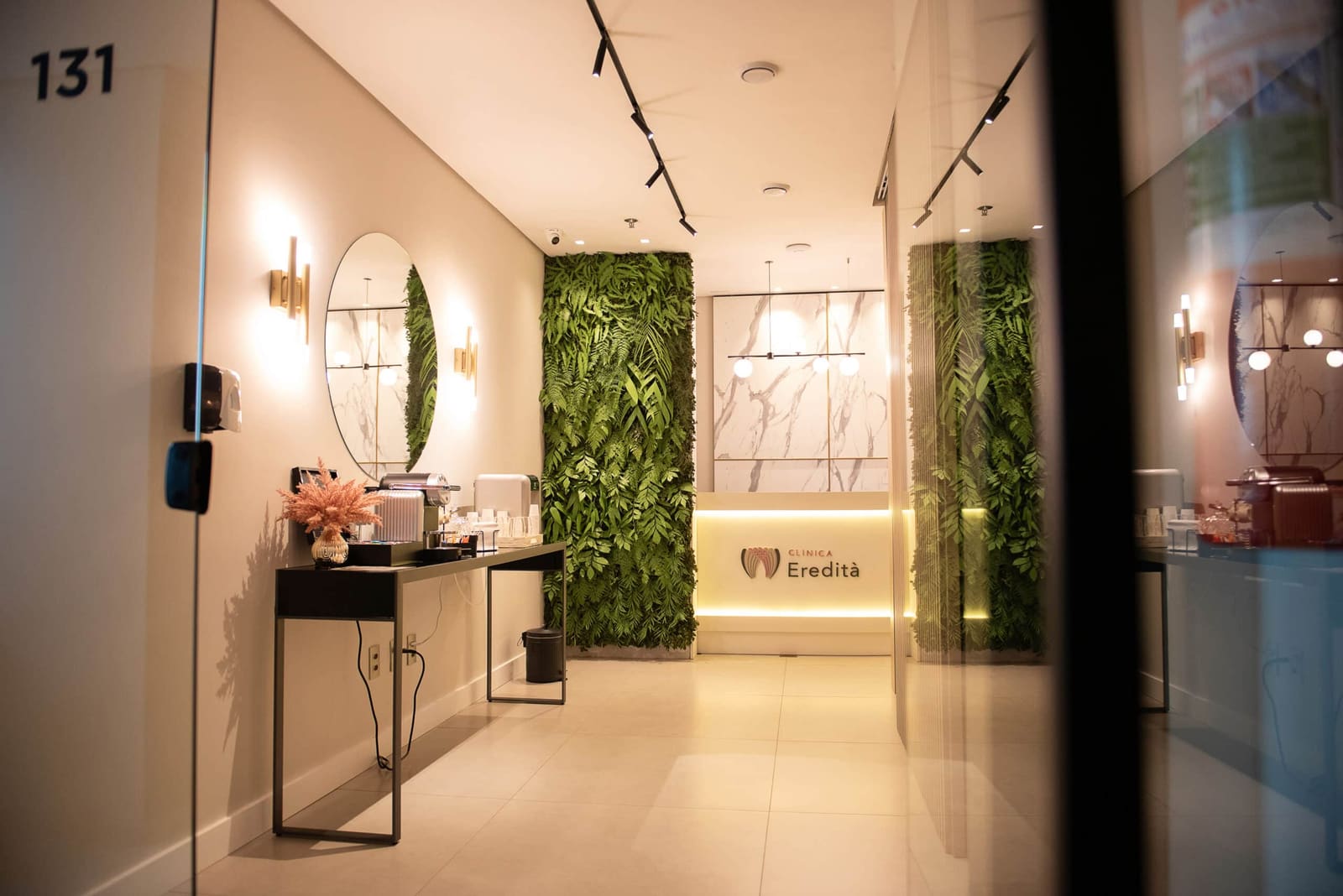 Recepção da unidade Funchal com parede de plantas naturais, espelho e iluminação premium